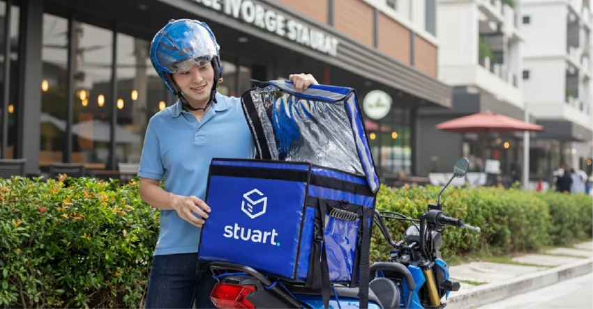 A Stuart delivery person with their motorcycle and delivery bag